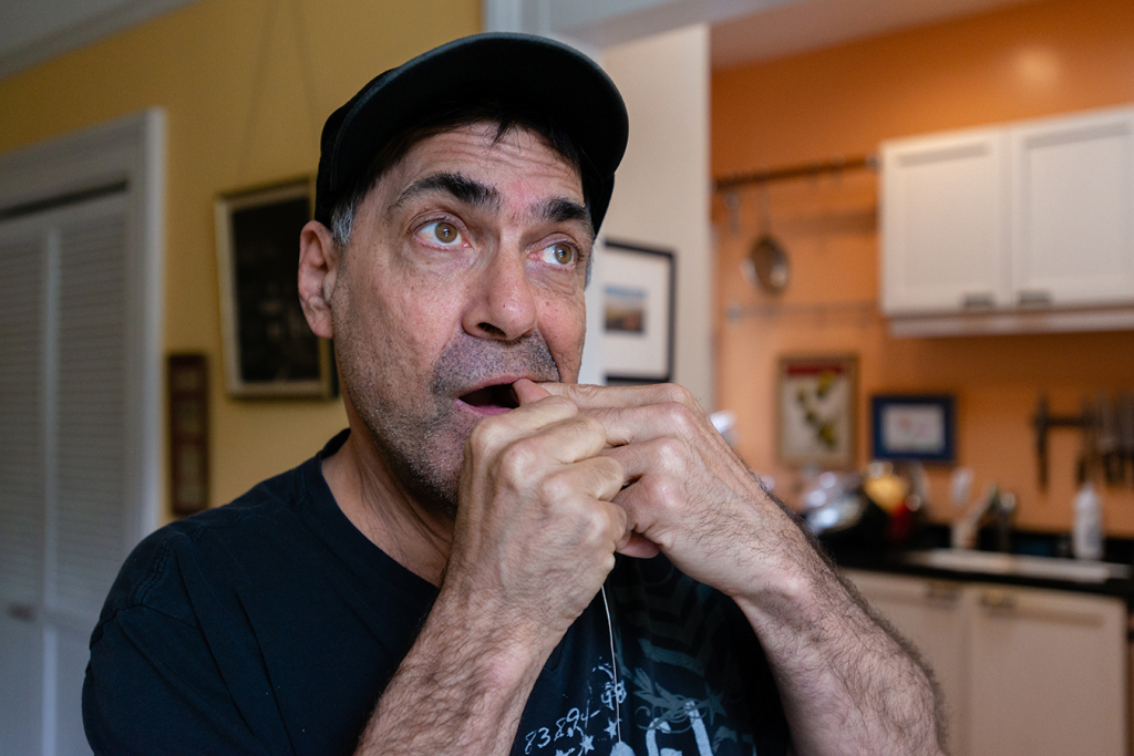 David Tuller flosses his teeth as he walks around his San Francisco home. After he was diagnosed with periodontal disease, Tuller underwent several extractions, titanium implants in his jaw, multiple bone grafts and a series of gum surgeries. (Heidi de Marco/KHN)